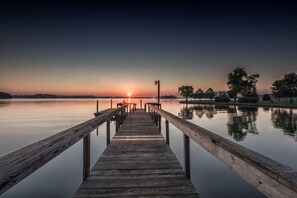 Eine Holzstege, der sich in ruhiges Wasser erstreckt, mit einem Sonnenuntergang im Hintergrund.