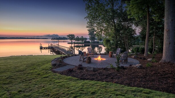 A lakeside patio with a fire pit, seating, and a dock extending into the water.