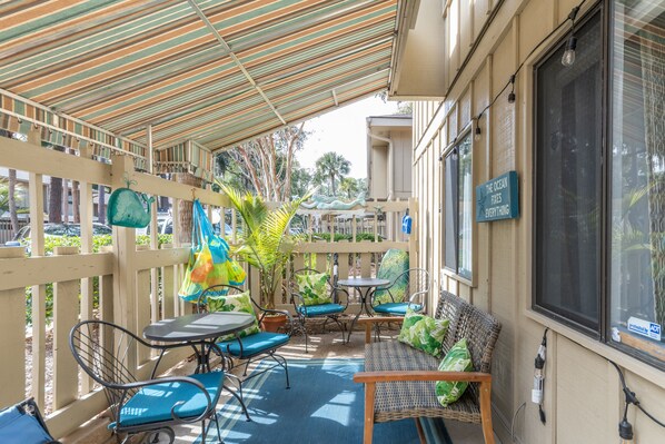 An outdoor patio with wicker furniture, a striped awning, and a sign reading "The Ocean Fixes Everything".
