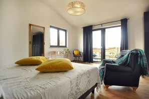 Een slaapkamer met een bed, een stoel, een bureau en een groot raam.