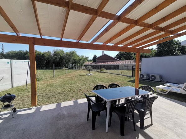 Un patio couvert avec une table et des chaises, un barbecue et deux unités de climatisation.