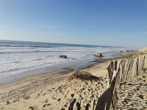 A sandy beach with a wooden fence, waves, and distant rocks. - New House Between the Lake and the Ocean (Naujac-sur-Mer)