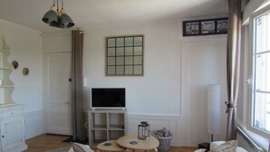 Un salón con sofá, televisor, una mesita y una ventana con cortinas.