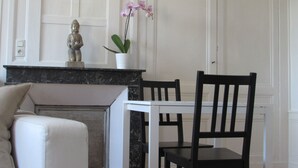 Un comedor con una mesa y sillas blancas, una estatua en la chimenea y una orquídea en maceta.