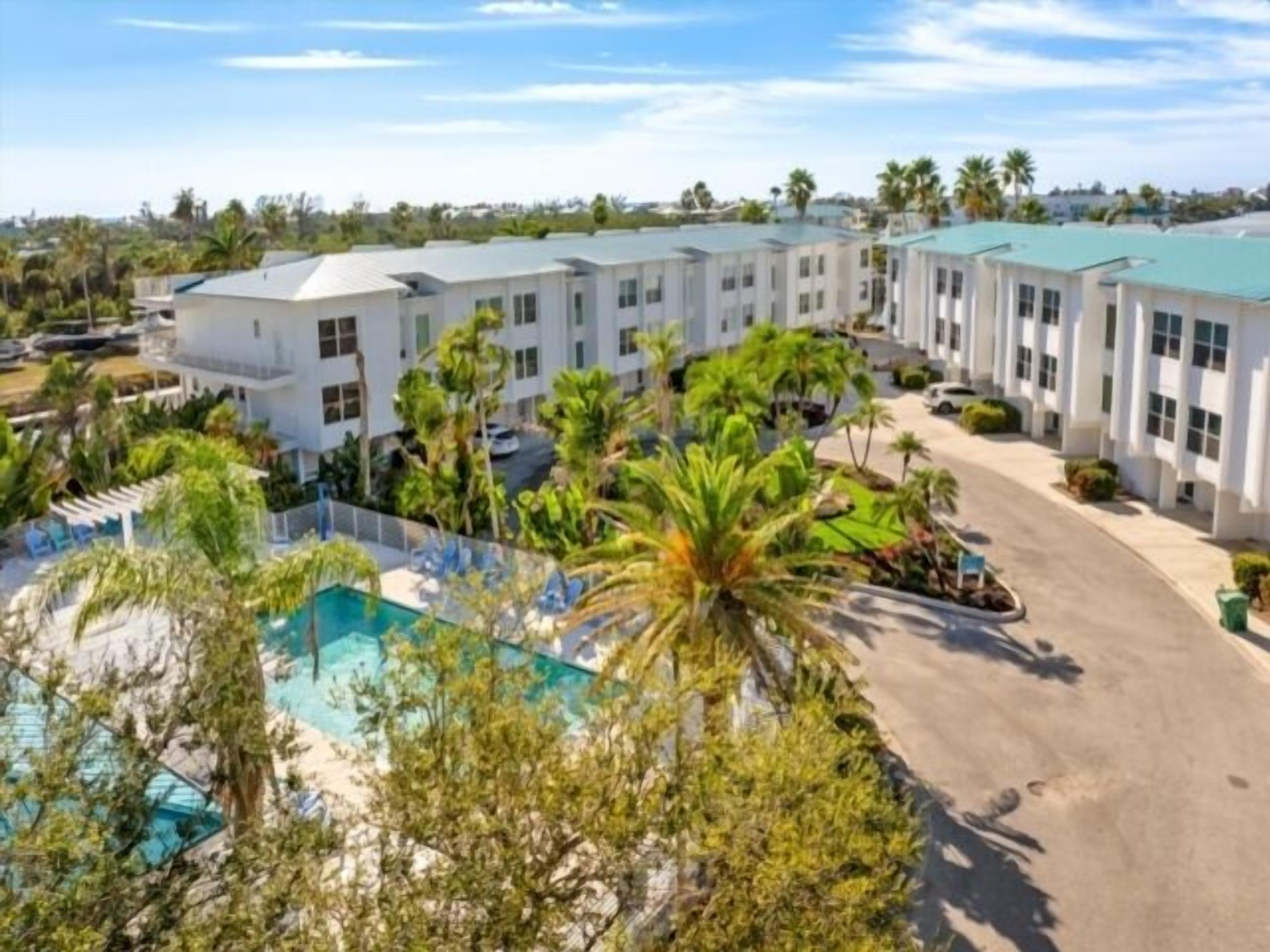 A hotel with a pool surrounded by palm trees and a parking area.