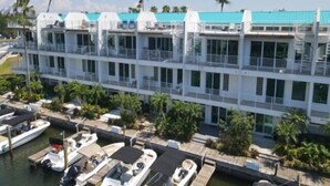 Een meerlaags hotel met balkons, een jachthaven met boten en palmbomen.