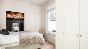 A bedroom with a bed, a bookshelf, a fireplace, and a large window.