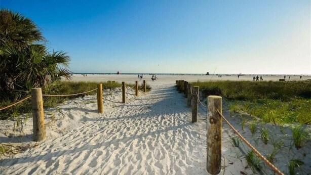 Un sentiero sabbioso che costeggia la spiaggia, con pali e corde di legno, conduce verso l'oceano.