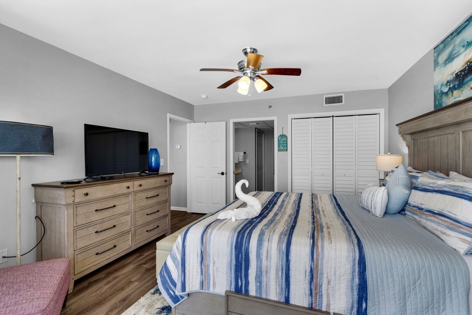 A bedroom with a bed, a dresser, a television, a ceiling fan, and a door.