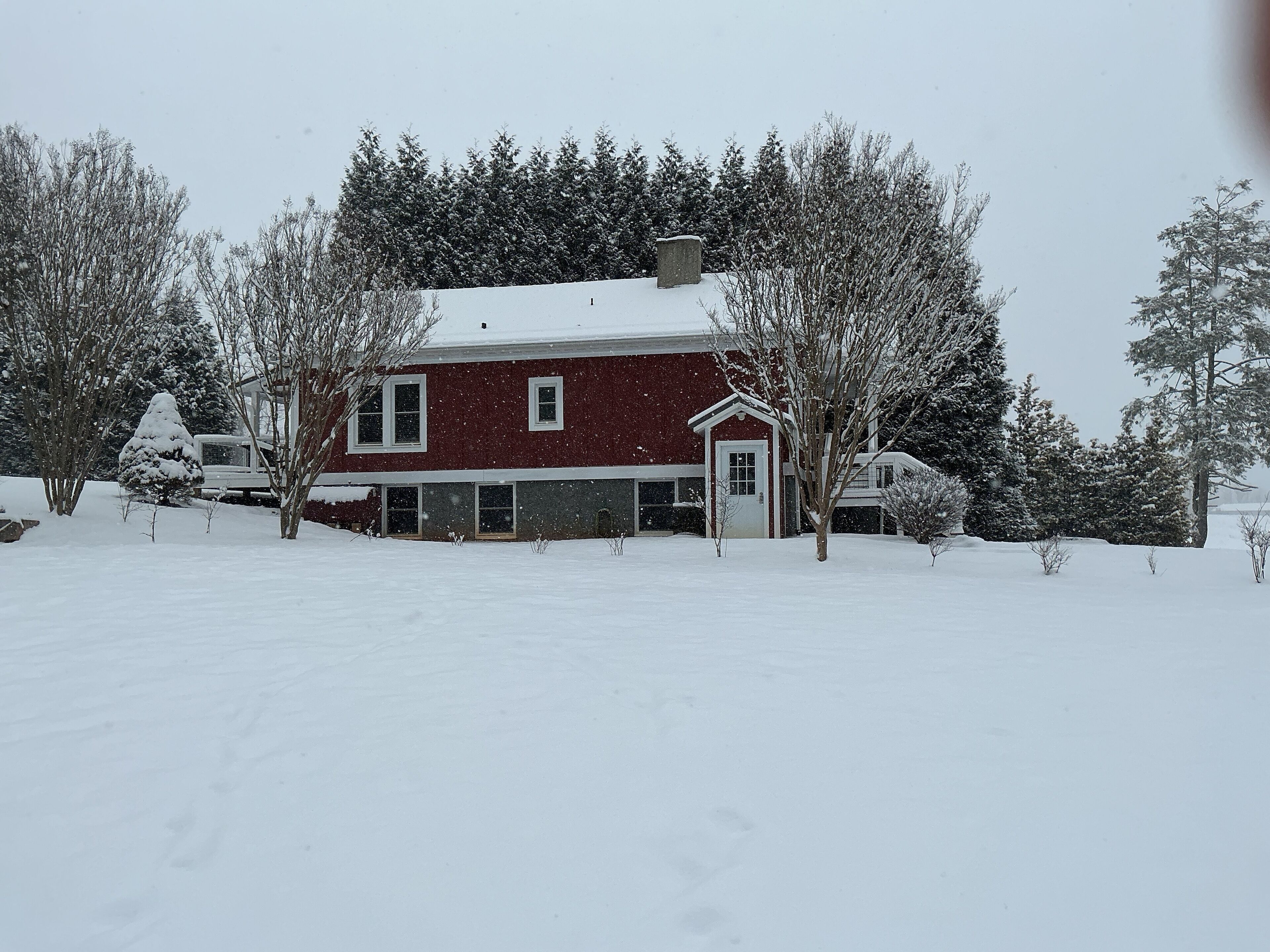 Ein zweistöckiges Haus mit roter Fassade und weißer Tür, umgeben von schneebedeckten Bäumen und einer verschneiten Landschaft.