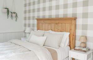Een netjes opgemaakt bed met een houten hoofdeinde, een bedlampje en een klein nachtkastje met een boek en een lamp.