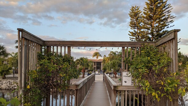 A wooden deck leading to a building with a 'NO FISHING' sign, surrounded by greenery and palm trees. - 1st floor Ft. Myers Davis Lake Condo, minutes to Sanibel and Fort Myers beach (Fort Myers)
