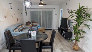 A modern living room with a round dining table, black chairs, a sofa with decorative pillows, a television, and a large potted plant. - 1st floor Ft. Myers Davis Lake Condo, minutes to Sanibel and Fort Myers beach (Fort Myers)