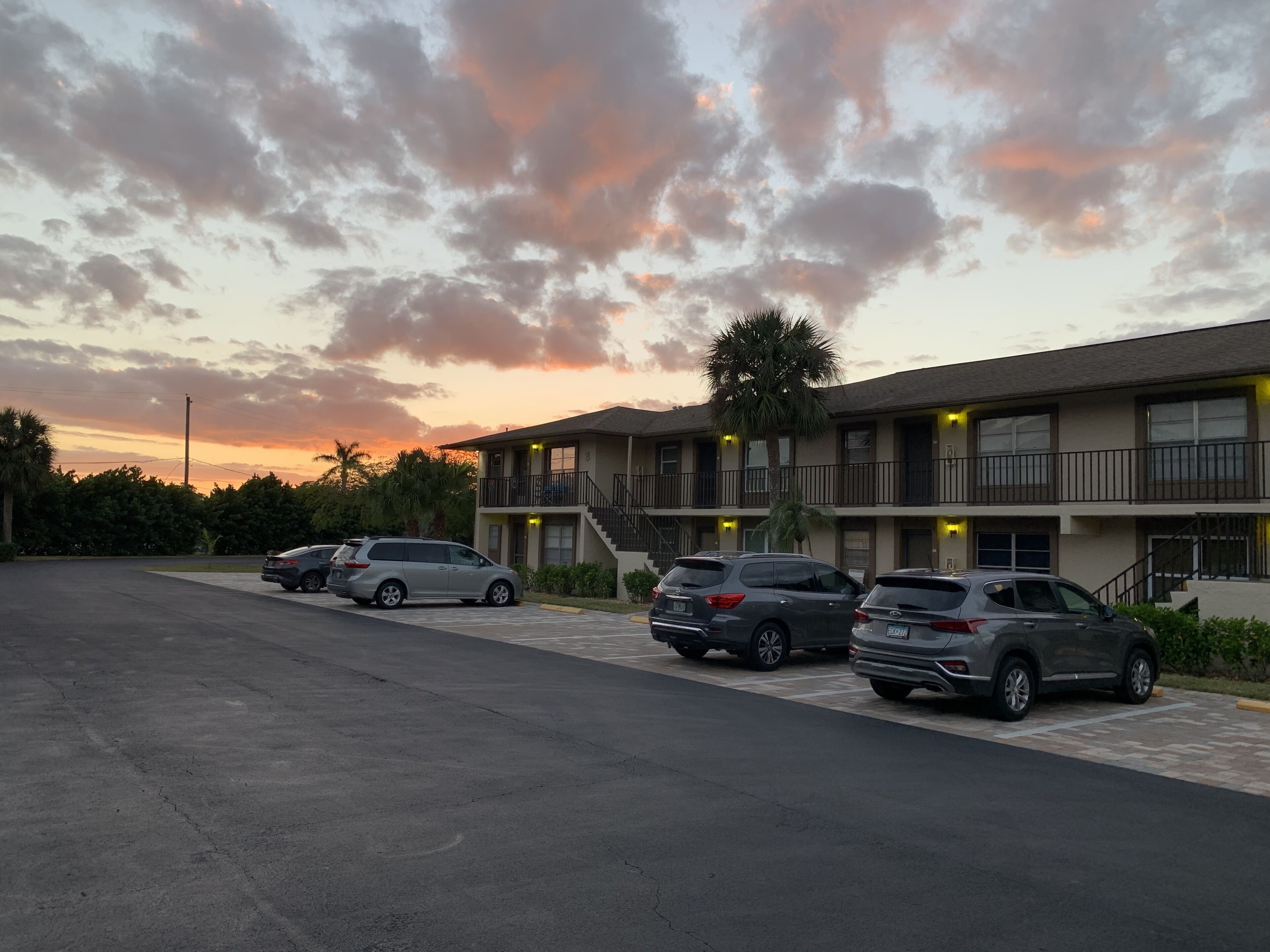 A motel with a two-story structure, a parking lot, and a sunset sky.