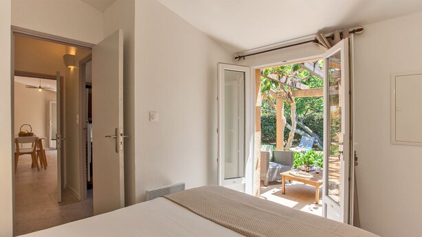 A bedroom with a bed, a door leading to a balcony with outdoor furniture, and a view of greenery. - maison kiwi avec piscine chauffée  terrasse  jardin et bbq à Calvi (Calvi)