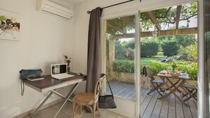 A room with a desk, laptop, chair, and a view of a garden through a glass door. - minivilla lilas indépendante à Calvi avec jardin et piscine, jardin et bbq (Calvi)