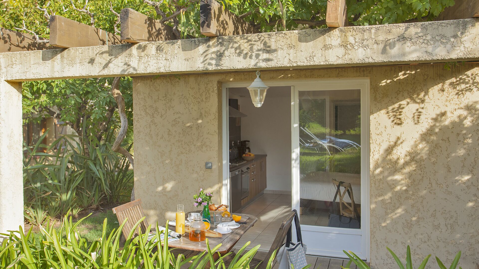 A small, enclosed outdoor dining area with a table set for breakfast, a wooden chair, and a glass door leading to a kitchen.