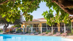 A poolside area with lounge chairs, a clear blue pool, and a building with large windows and a tiled roof. - minivilla lilas indépendante à Calvi avec jardin et piscine, jardin et bbq (Calvi)