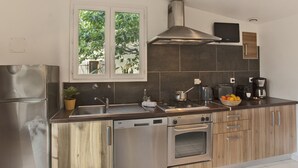 A modern kitchen with stainless steel appliances, a built-in oven, a gas stove, and a large window with a view of greenery. - minivilla lilas indépendante à Calvi avec jardin et piscine, jardin et bbq (Calvi)