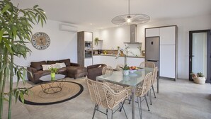 Un salon moderne avec un canapé en cuir marron, une table à manger en verre et des chaises en osier, ainsi qu’une grande horloge murale.