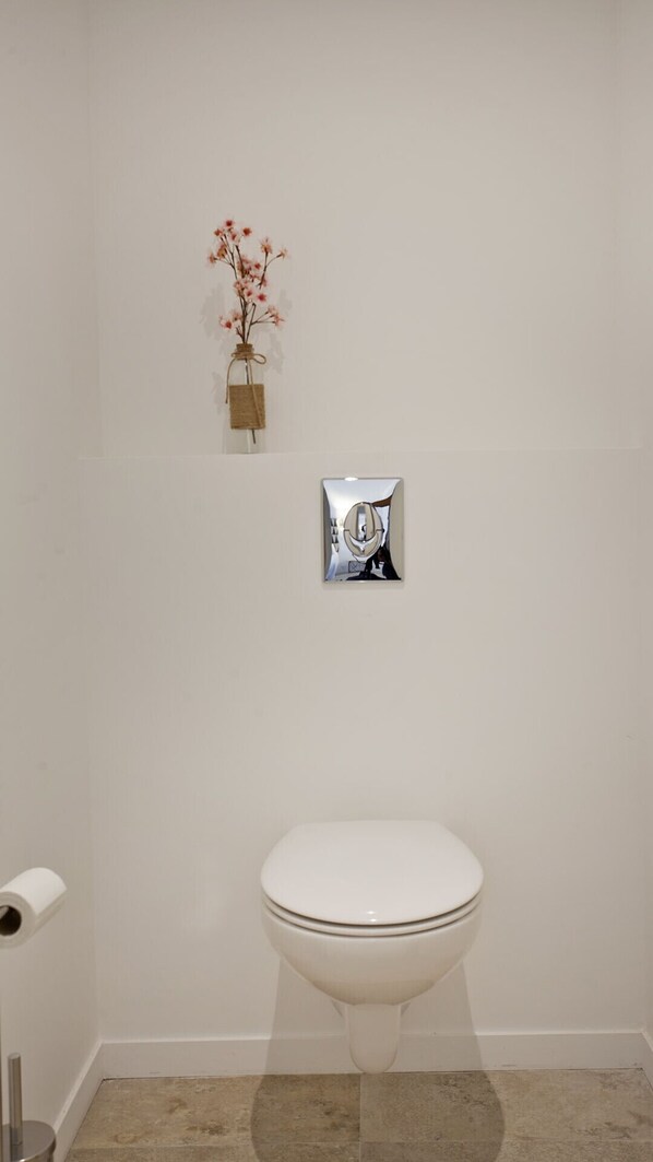 A bathroom with a white toilet, a small vase with dried flowers, and a mirror with a chrome frame.