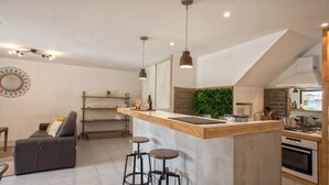 A modern kitchen with a wooden island, bar stools, and a dining area with a sofa and a mirror. - location de vacances figuier avec jardin barbecue piscine chauffée à Calvi (Calvi)