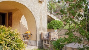 An outdoor patio with a stone archway, a small table with fruits and a bottle, and a potted plant. - location de vacances figuier avec jardin barbecue piscine chauffée à Calvi (Calvi)