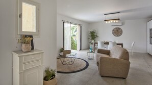 A modern living room with a sofa, a dining table with chairs, a kitchen area, and a large window with curtains.