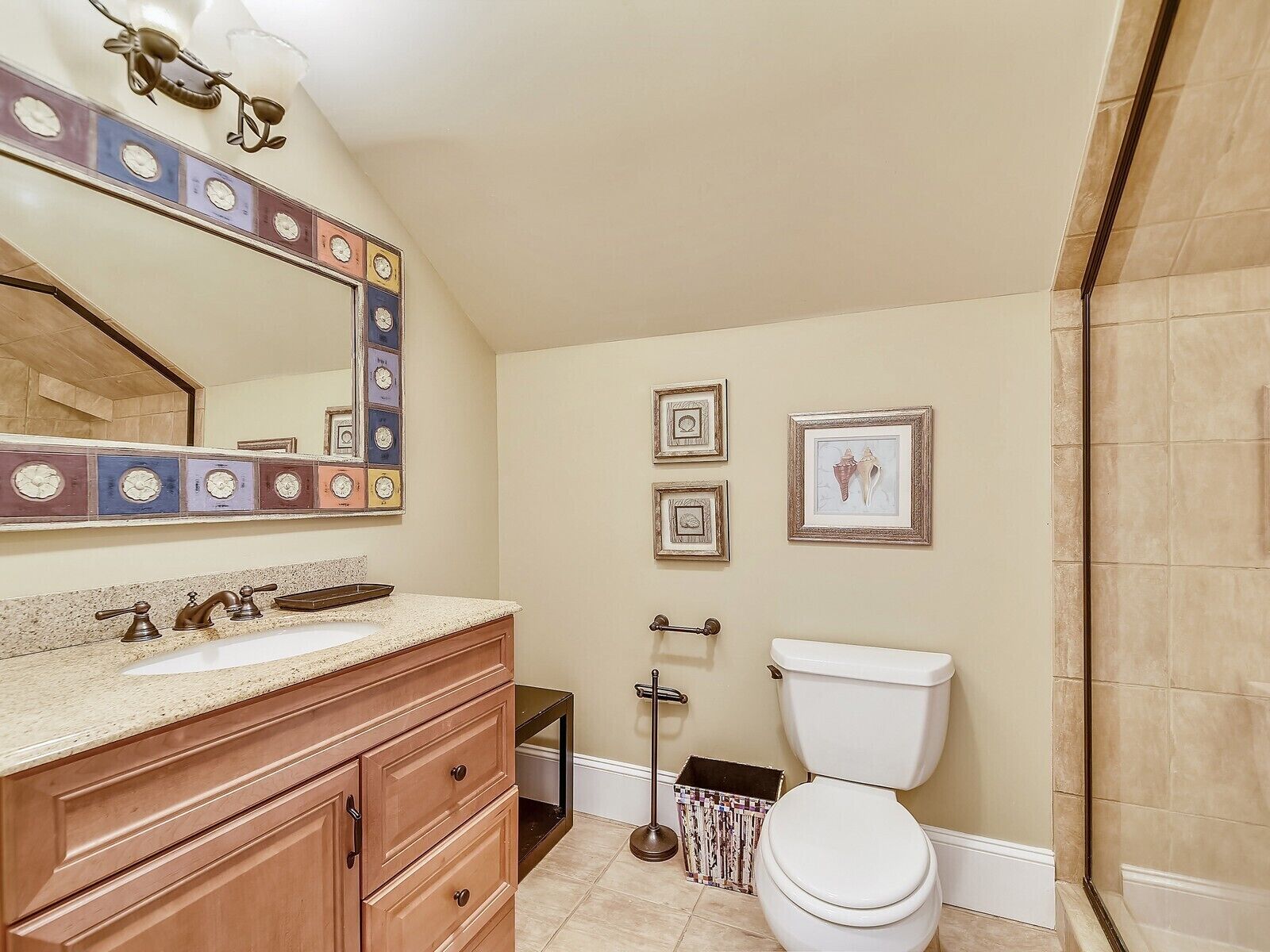 A bathroom with a vanity, sink, mirror, toilet, and framed pictures on the wall.