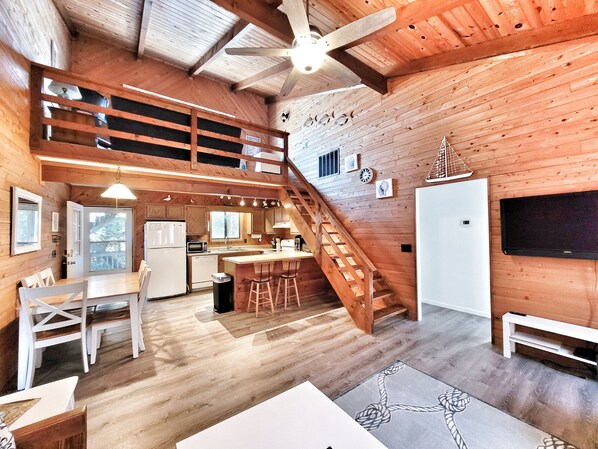 A spacious cabin with a wooden interior, a kitchen area, a dining space, and a staircase leading to an upper level.
