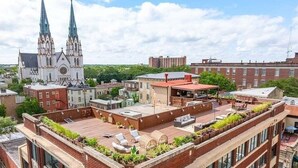 Terraço no telhado com área de estar e plantas, com vista para uma paisagem urbana que inclui uma igreja imponente e edifícios residenciais.