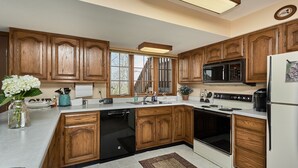 A kitchen with wooden cabinets, a built-in microwave, a refrigerator, and a large window. - Get away from it all (Foristell)