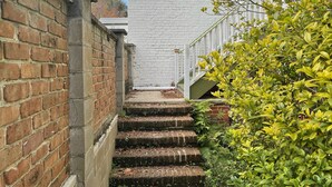Eine schmale Ziegelstein-Treppe führt zu einem weißen Gebäude mit weißem Geländer.