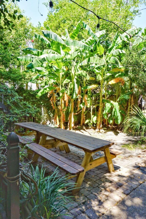 Une table de pique-nique en bois, située dans un jardin agrémenté de bananiers et de diverses plantes.