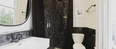 A bathroom with a white sink, black and white checkered floor, a white toilet, and a shower with a black curtain.