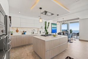 A modern kitchen with a central island, stainless steel appliances, pendant lighting, and a view to the outdoors.