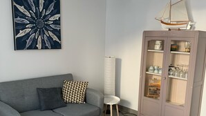 A living room with a grey sofa, a white coffee table, a yellow armchair, a cabinet with glass doors, and a hanging rattan light fixture. - Maison sur ÎLE DE RÉ (Ars-en-Ré)