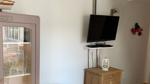 A living room with a yellow armchair, a television on a stand, a cabinet, and a glass-fronted cabinet with items inside. - Maison sur ÎLE DE RÉ (Ars-en-Ré)