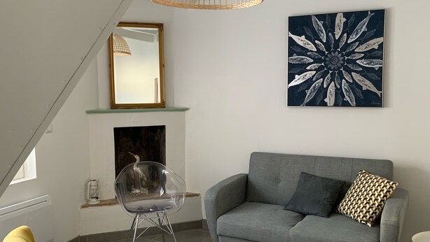 A modern living room with a grey sofa, yellow armchairs, a clear glass chair, a white coffee table, a woven pendant light, a fireplace, and a large abstract painting. - Maison sur ÎLE DE RÉ (Ars-en-Ré)