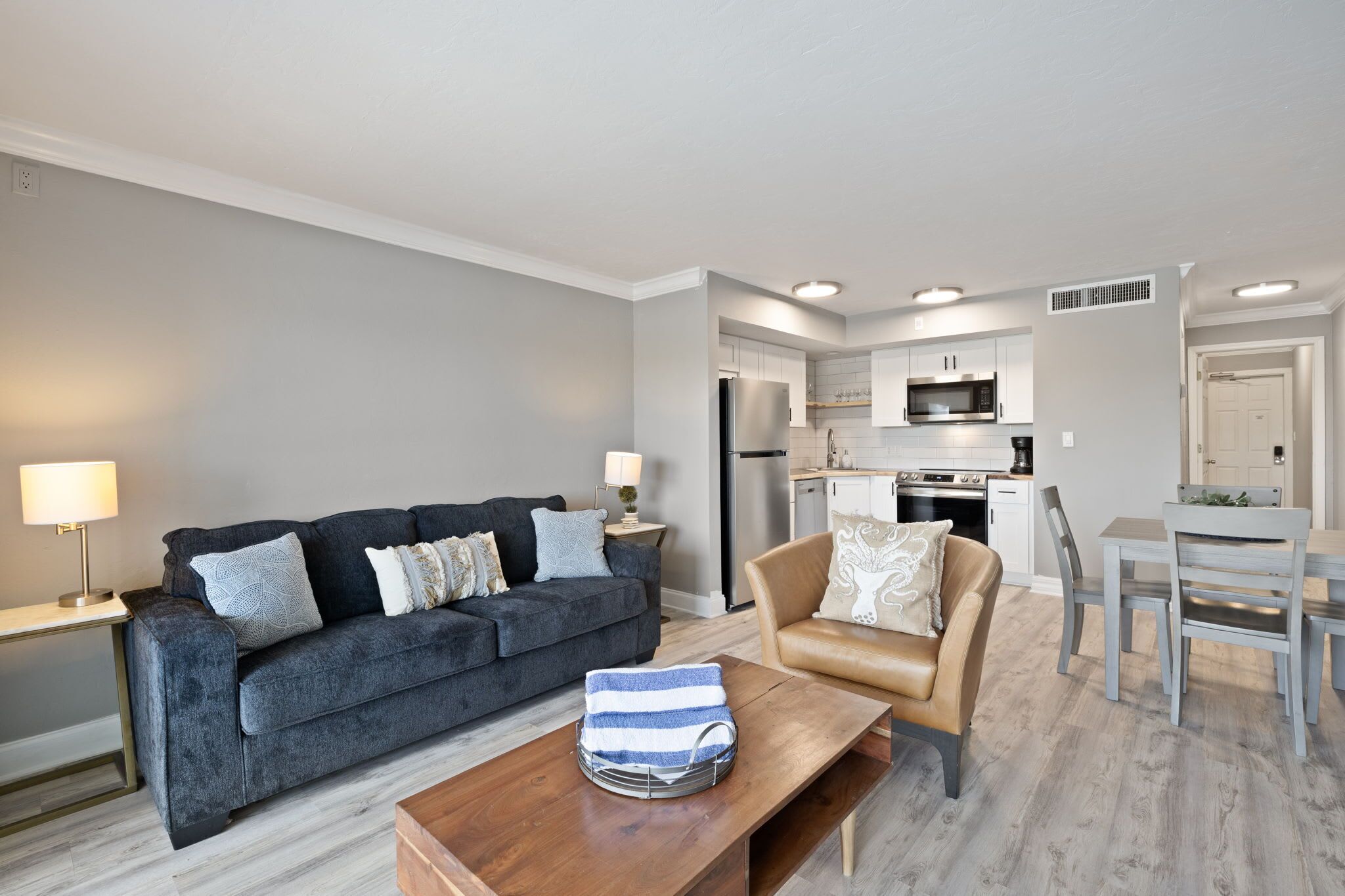 A modern living room with a sofa, a coffee table, a dining table with chairs, and a kitchen area with appliances.