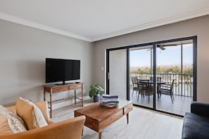 A living room with a TV, a wooden coffee table, a sofa, and a balcony with outdoor furniture.
