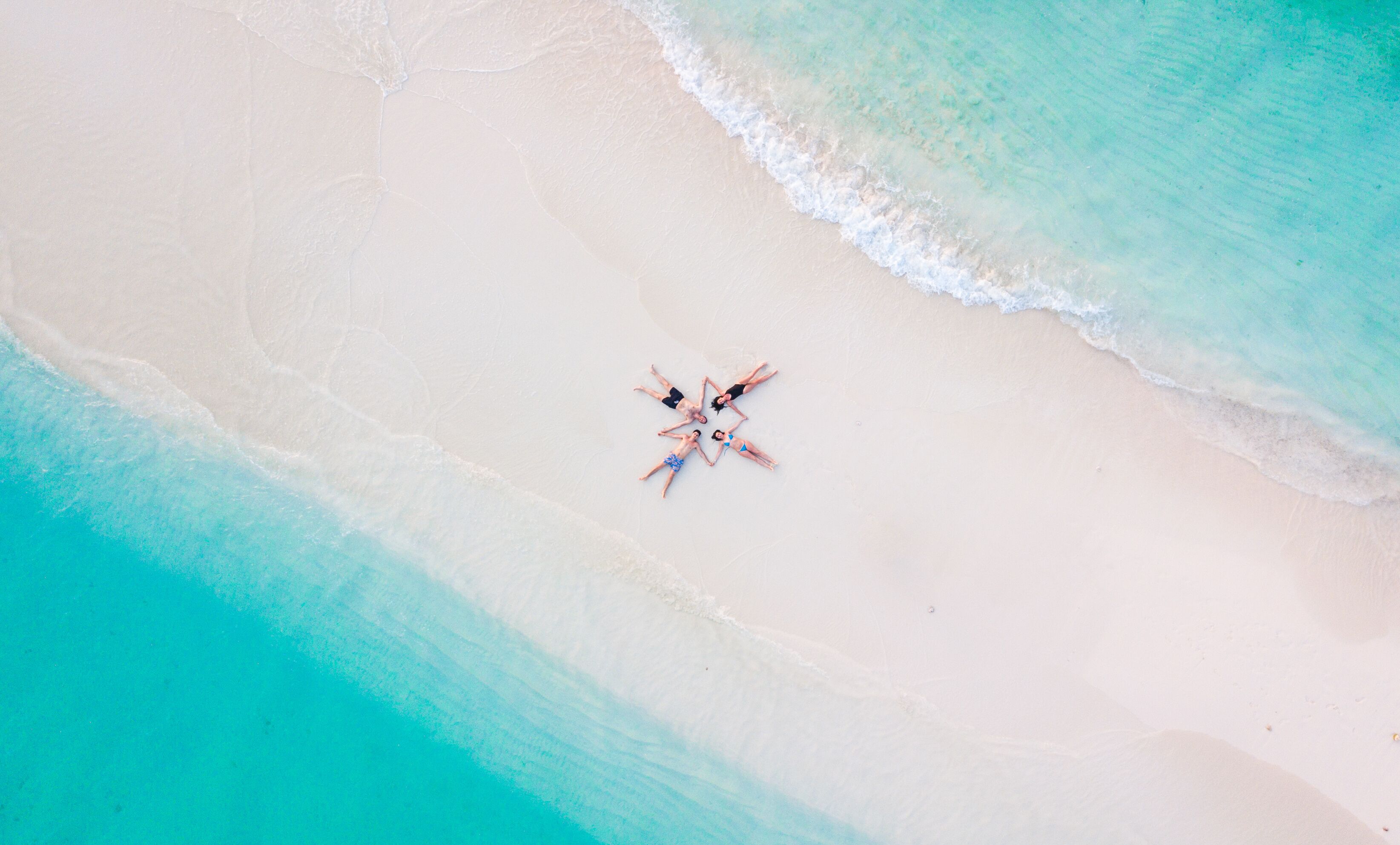 An aerial view of a beach with four people lying in a star formation.
