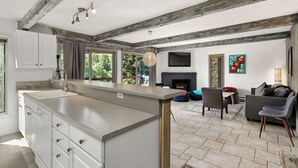 A modern kitchen with a large island, white cabinetry, and a stone backsplash. There is a dining area with a table and chairs, and a living room with a sofa and a fireplace. - BRAND NEW REMODEL, Gorgeous 2BR 2BA Mountain Side Condo, Hot Tub, Fireplace, EPI (Snowmass Village)