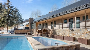 A pool area with a stone wall, a wooden deck, and a covered seating area with a staircase. - BRAND NEW REMODEL, Gorgeous 2BR 2BA Mountain Side Condo, Hot Tub, Fireplace, EPI (Snowmass Village)