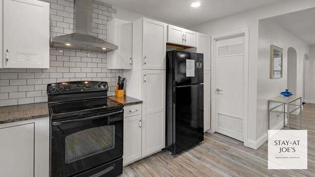 A modern kitchen with white cabinets, a black stove, and a black refrigerator.