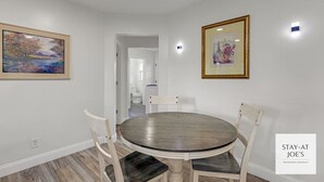 A dining area with a round table and four chairs, a painting on the wall, and a framed picture above the table.