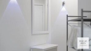 A modern bathroom with a white sink, mirror, and towel rack. There are two wall-mounted lights and a visible towel rack.