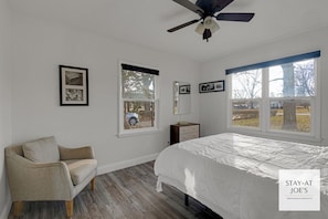 A bedroom with a bed, a chair, two windows, a ceiling fan, and framed pictures on the wall. - Private 4 BDRM house, 5 Miles from Downtown #6 (Indianapolis)