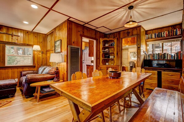 A wooden interior with a dining table, leather sofa, and bookshelves.