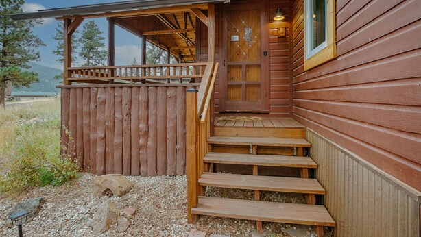 Een houten hut met een veranda, een trap en een deur met een raam.